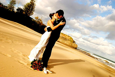 Picture Of Bride And Groom Kissing On The Beach With The Sun Shining On Them