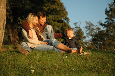 Family of three sitting on the grass in the park enjoying the Sun