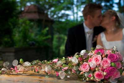 A Bouquet Of Wedding Flowers Is In The Foreground While The Bride And Groom Are Kissing In The Background
